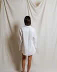 Person wearing a white shirt standing in front of a plain white curtain