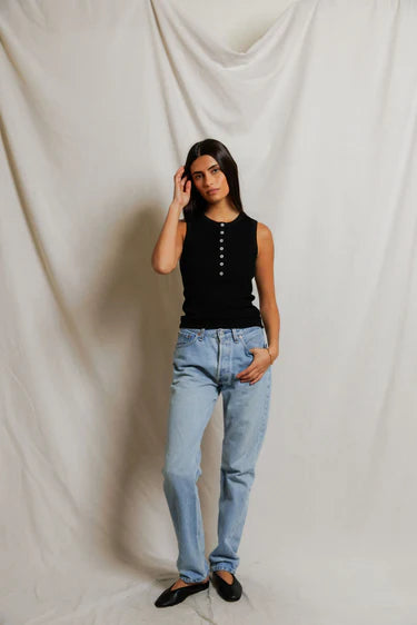 Woman wearing a black top and light blue jeans against a plain background