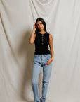 Woman wearing a black top and light blue jeans against a plain background