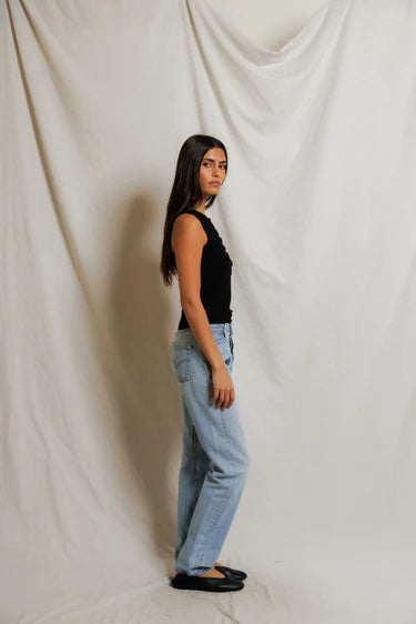 Woman wearing a black sleeveless top and blue jeans against a plain background