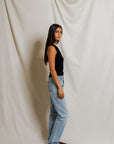 Woman wearing a black sleeveless top and blue jeans against a plain background