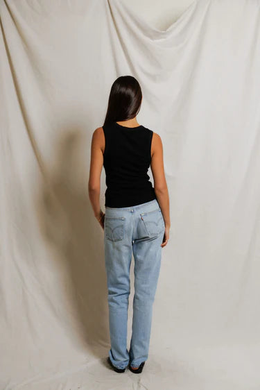 Person wearing a black top and light blue jeans standing against a plain white background