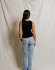 Person wearing a black top and light blue jeans standing against a plain white background