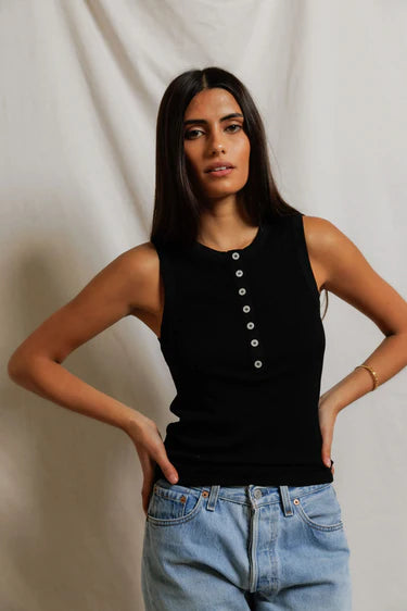 Woman wearing a black sleeveless top and blue jeans against a plain background