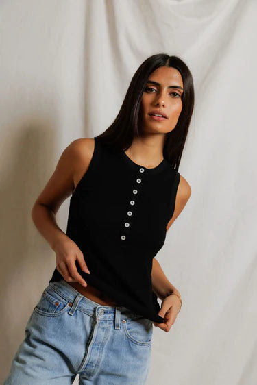 Woman wearing a black sleeveless top and blue jeans against a plain background