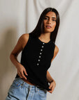 Woman wearing a black sleeveless top and blue jeans against a plain background