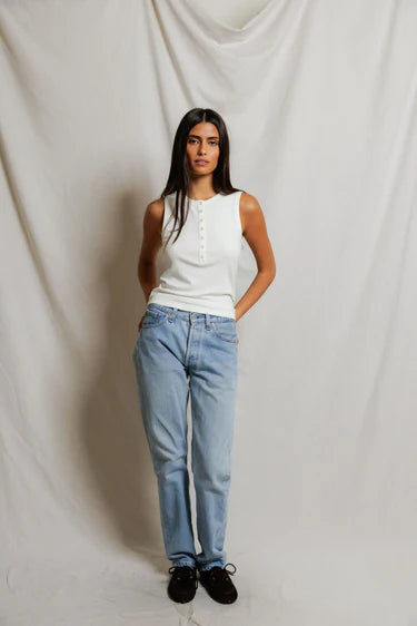 Woman wearing a white sleeveless top and light blue jeans against a plain background