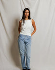 Woman wearing a white sleeveless top and light blue jeans against a plain background