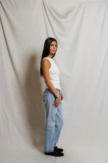 Woman wearing a white sleeveless top and light blue jeans against a plain background