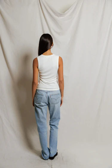 Person wearing a white sleeveless top and light blue jeans against a plain background