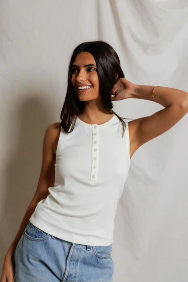 Woman wearing a white sleeveless top and blue jeans against a neutral background