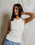 Woman wearing a white sleeveless top and blue jeans against a neutral background