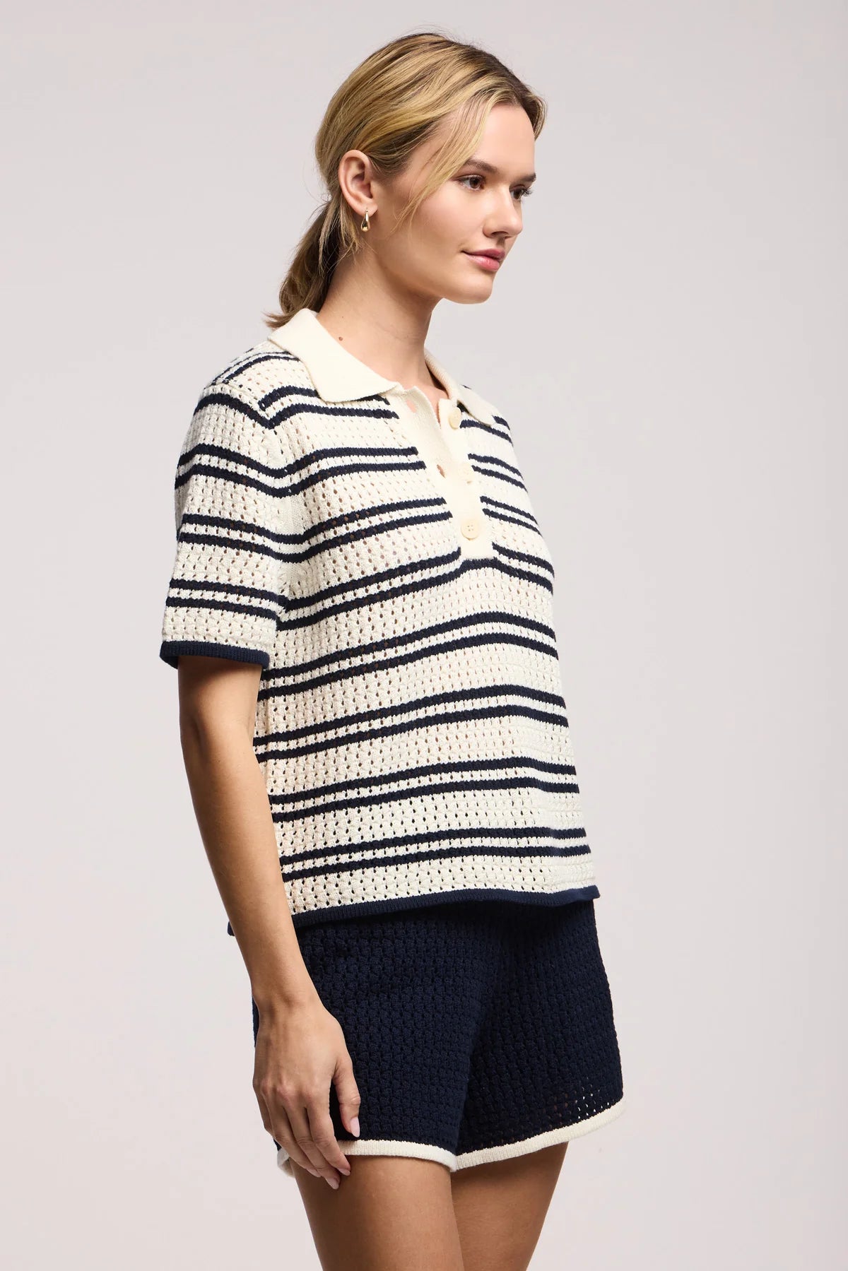 Model wearing the lumae milk and navy stripe short sleeve polo top with shorts on a white background, side