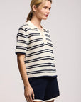 Model wearing the lumae milk and navy stripe short sleeve polo top with shorts on a white background, side