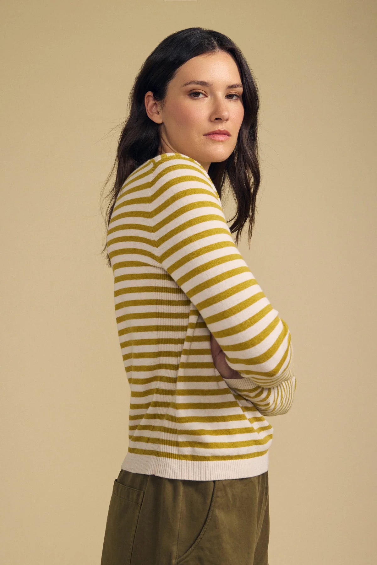 A woman modeling a yellow and white striped knit sweater, shown from a three-quarter back view against a solid beige studio background.