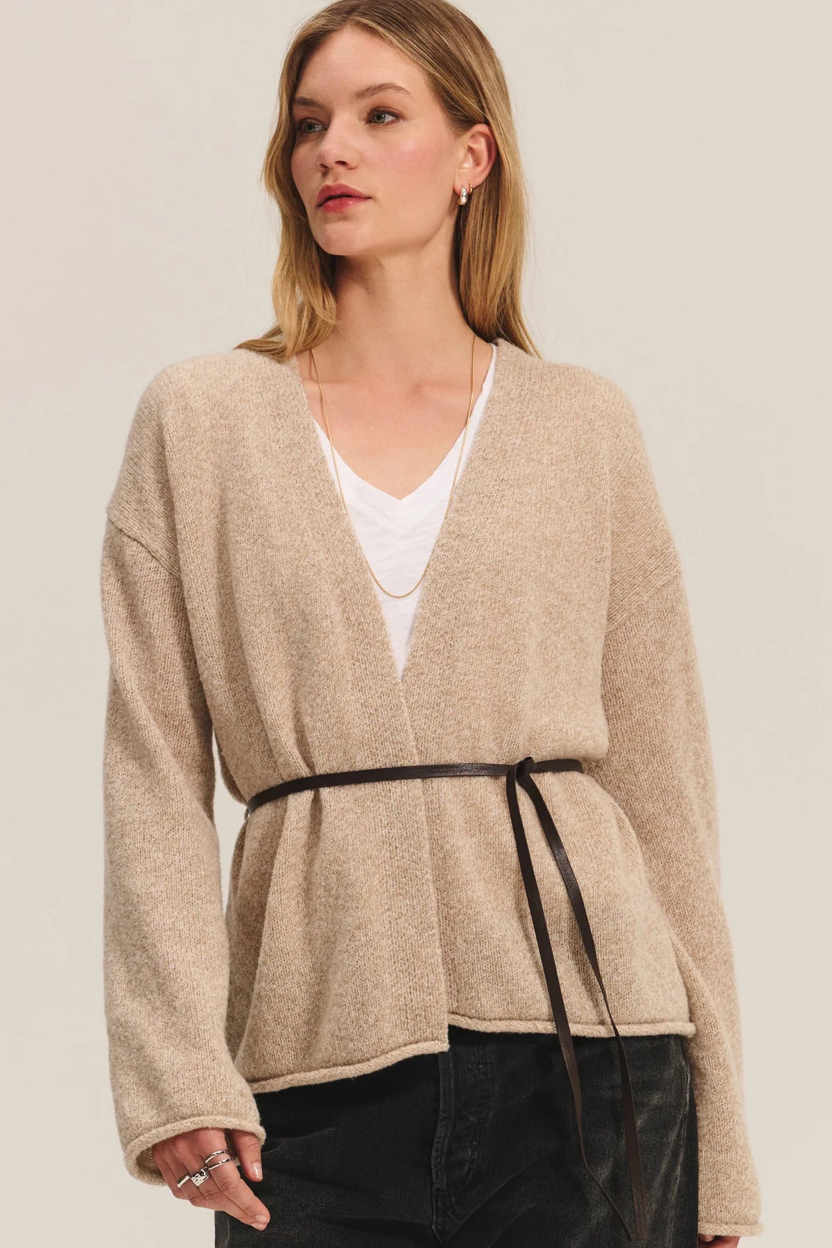 Woman wearing a beige wrap-style cardigan over a white top on a plain background