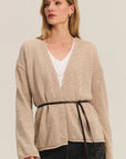 Woman wearing a beige wrap-style cardigan over a white top on a plain background