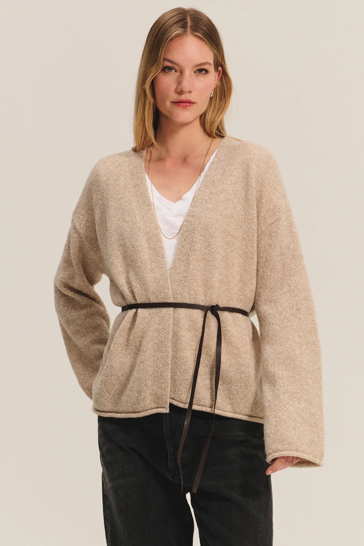 Woman wearing a beige cardigan with a belt on a plain background