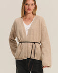 Woman wearing a beige cardigan with a belt on a plain background