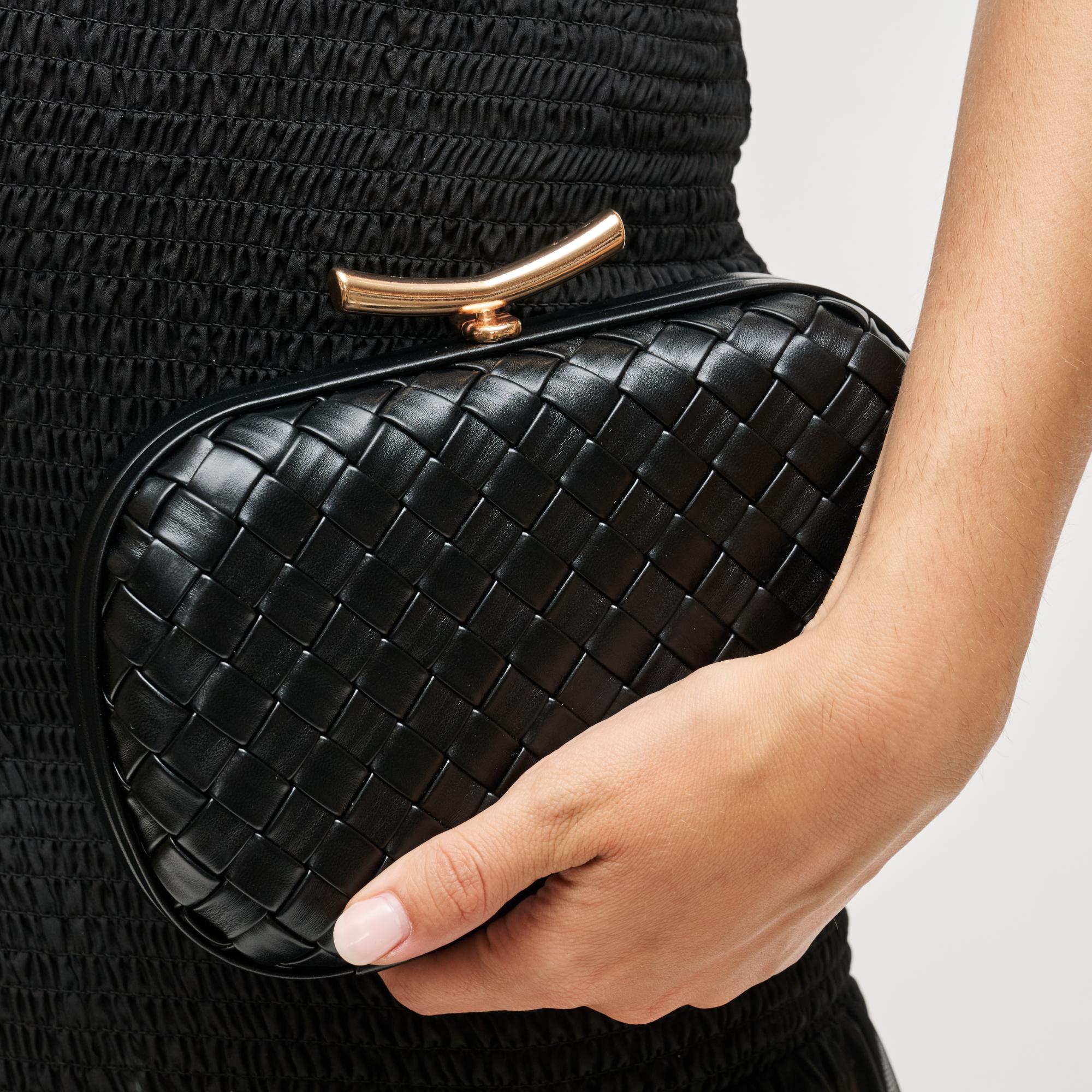 Black woven clutch held by a hand against a neutral background