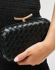 Black woven clutch held by a hand against a neutral background