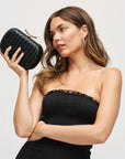 Woman holding a black woven clutch against a plain background