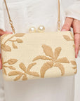 Beige handbag with floral embroidery held by a person wearing a white outfit.
