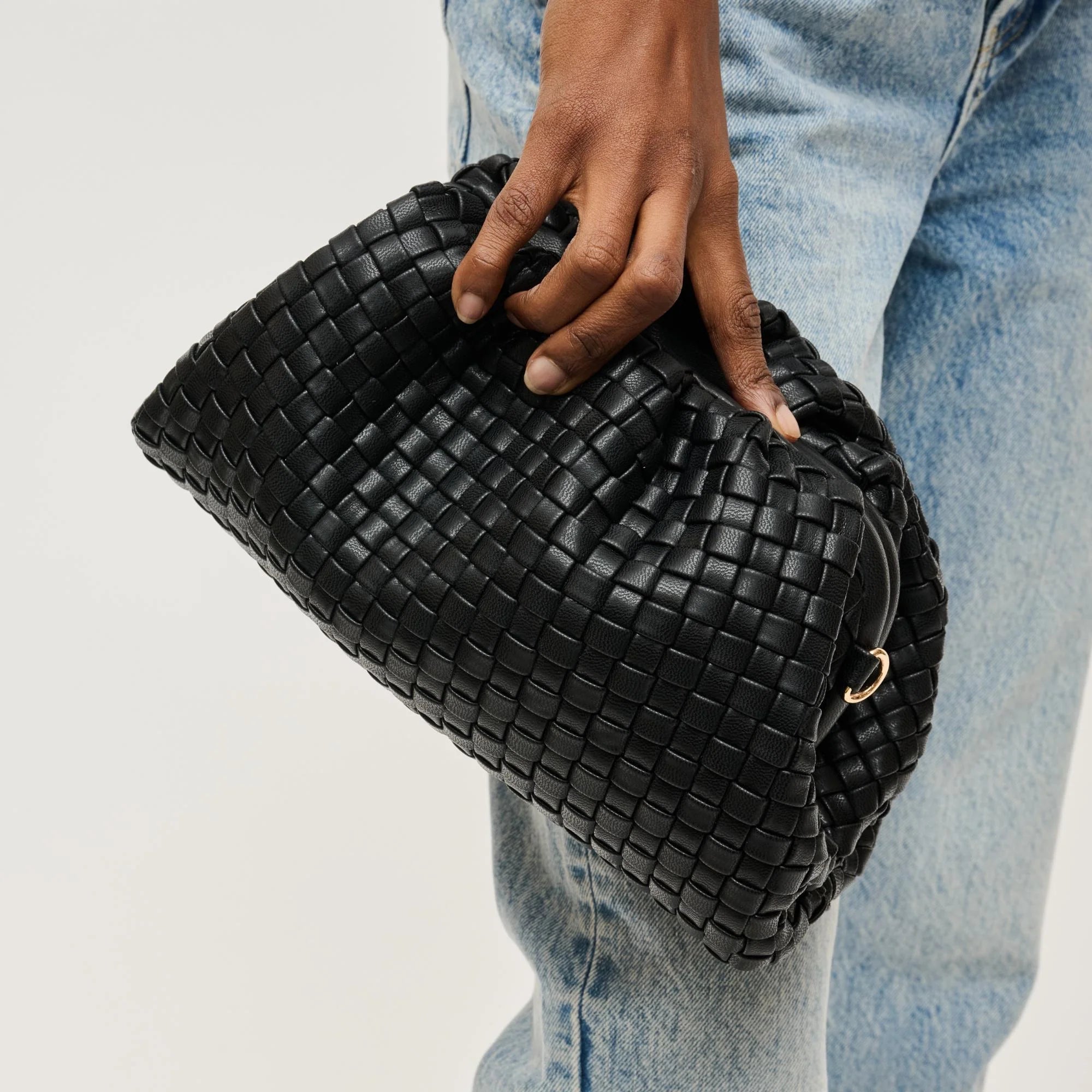 Black woven clutch held by a hand against a light background