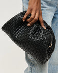 Black woven clutch held by a hand against a light background