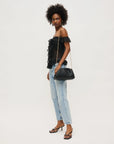 Woman wearing a black off-shoulder top and light blue jeans, holding a black handbag on a white background