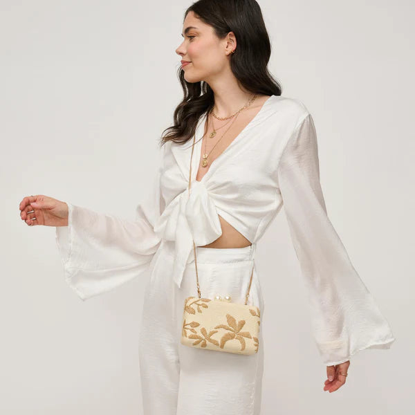 Woman in a white dress holding a beige handbag with floral patterns against a plain background