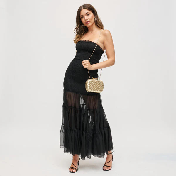 Woman wearing a black strapless dress with sheer panels and holding a gold clutch against a white background