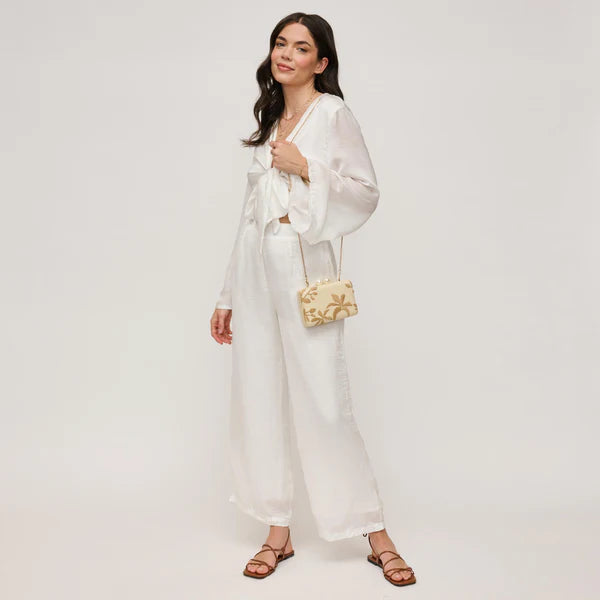 Woman in a white outfit holding a gold handbag on a plain background