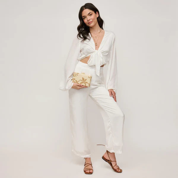 Woman in a white outfit holding a gold clutch against a plain background