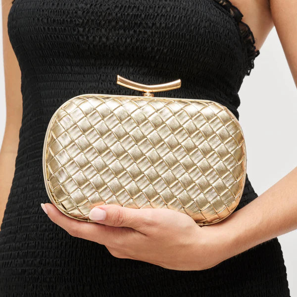 Gold woven clutch held by a person wearing a black dress.