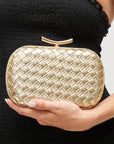 Gold woven clutch held by a person wearing a black dress.