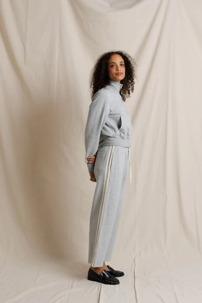 Woman wearing a light gray outfit against a plain background, side view