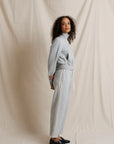 Woman wearing a light gray outfit against a plain background, side view