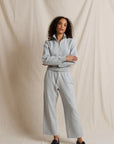 A woman modeling a light gray heathered two-piece loungewear set consisting of a quarter-zip long-sleeve top and matching wide-leg sweatpants, standing against a draped beige fabric backdrop.