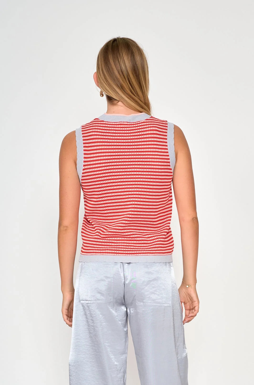 A woman shown from the back wearing a sleeveless red and white striped knit top with light gray trim, paired with light gray pants, against a plain light gray studio background.