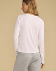 A woman shown from the back wearing a white long-sleeve top and light gray sweatpants, standing against a solid beige studio background.
