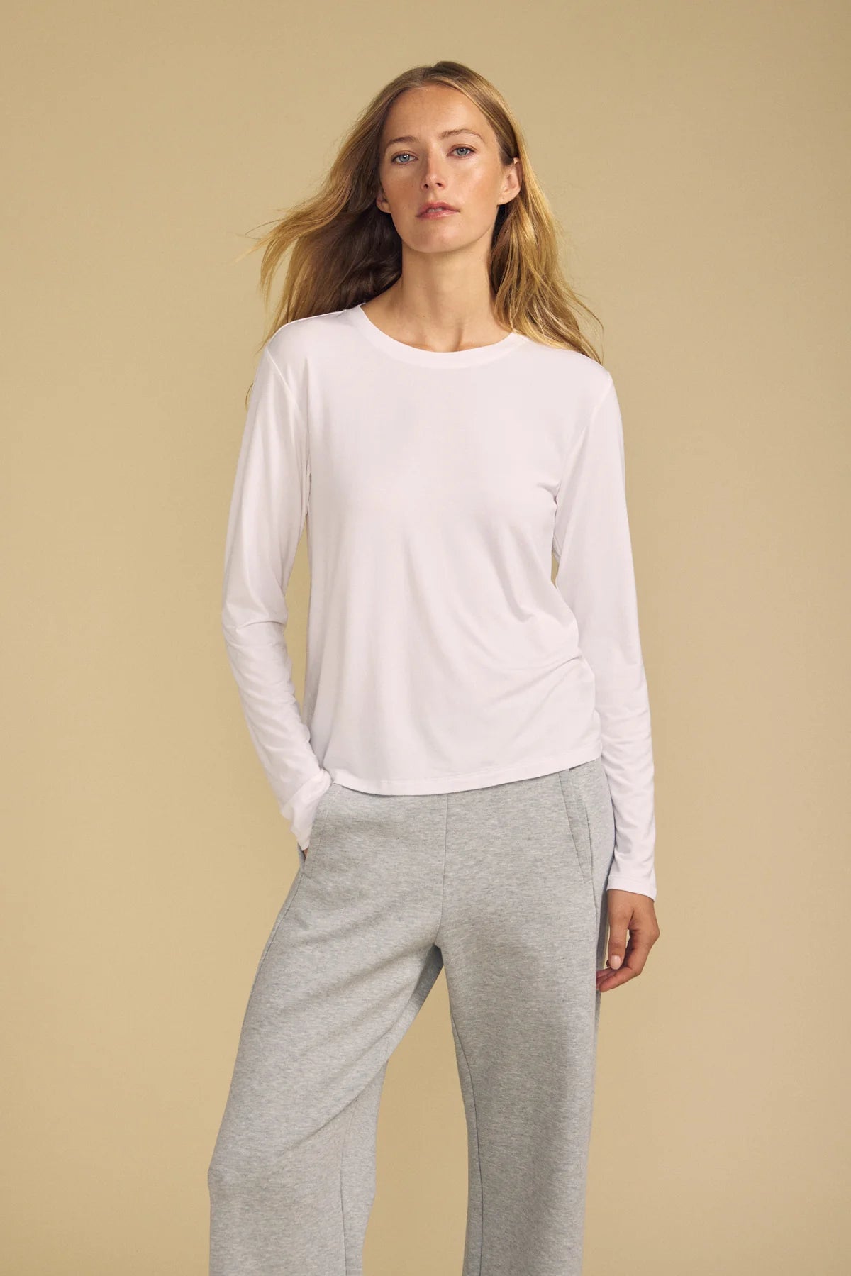model wearing a white long sleeve tee and gray sweatpants on a beige background