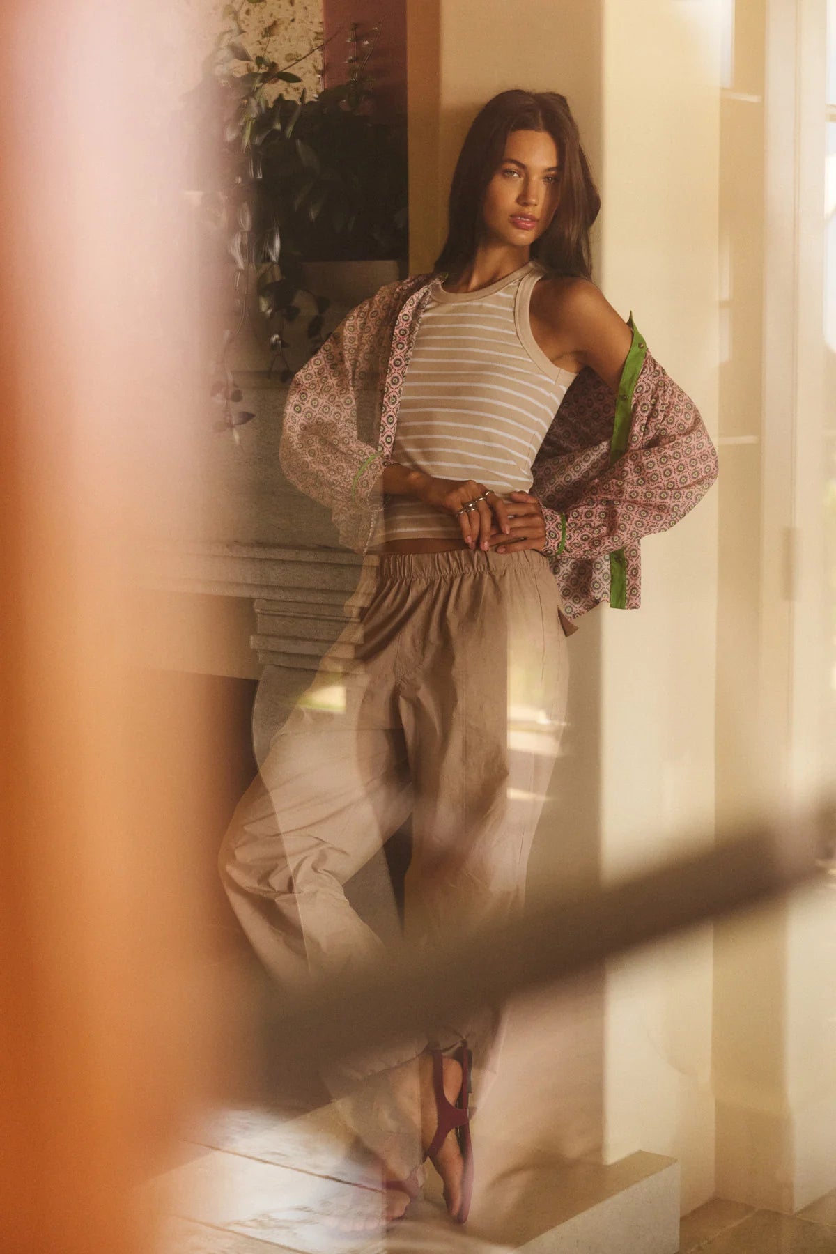 Woman standing in a softly lit room wearing a white top and beige pants.