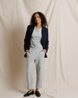 Woman wearing a dark blazer, light gray top, and pants against a plain background