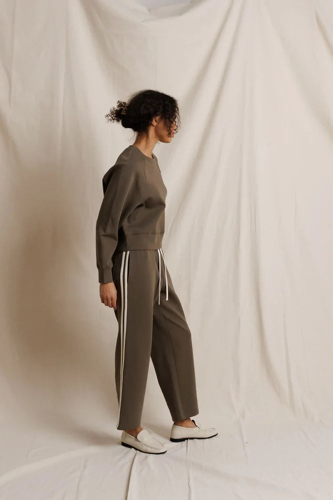 Person wearing a dark olive tracksuit with white stripes on a plain background