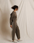Person wearing a dark olive tracksuit with white stripes on a plain background