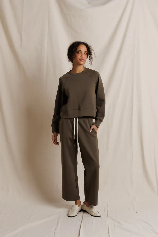 Woman wearing a dark oilve sweatshirt and pants against a beige background