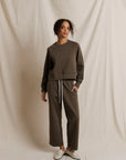 Woman wearing a dark oilve sweatshirt and pants against a beige background