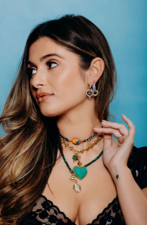 Woman wearing multiple necklaces and earrings against a blue background