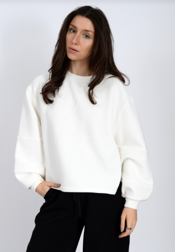 Woman wearing a white sweater and black pants against a plain background front view